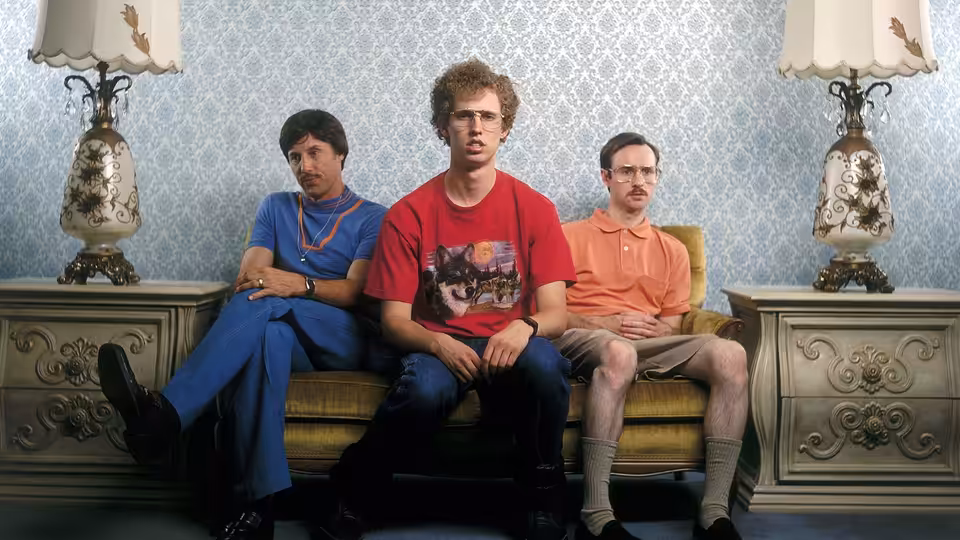 Napoleon Dynamite (Jon Heder) sits between Kip and Uncle Rico on a couch