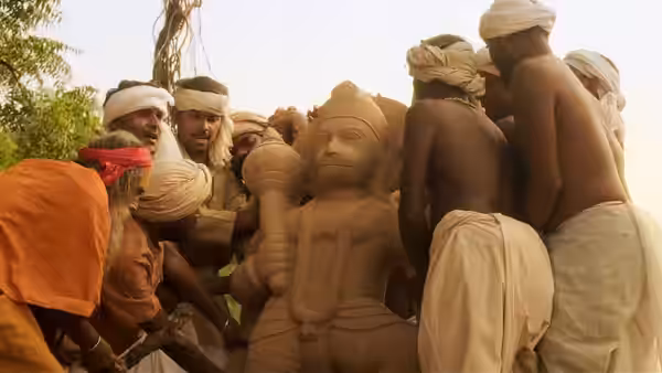 Men in turbans and dhotis gather around and carry a large Hanuman statue