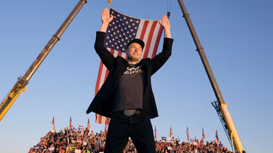 Elon Musk (Elon Musk) raises his arms before a crowd beneath a large American flag
