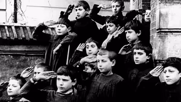 Schoolboys stand in rows, raising their hands in salute