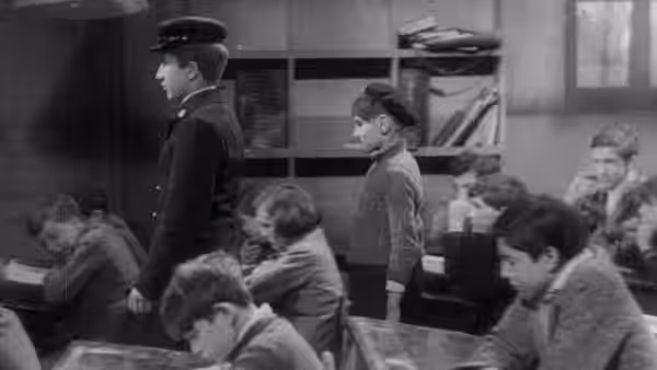 A supervisor walks between boys working at desks in a classroom