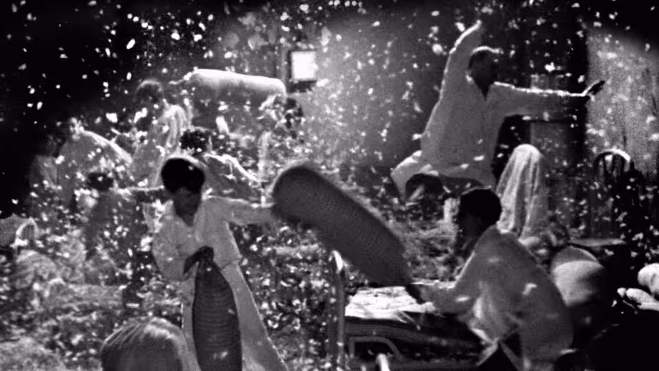 Boys in a dormitory throw pillows during a pillow fight