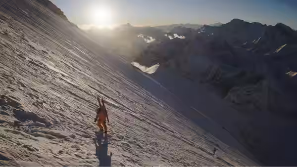A lone climber crosses a sunlit mountainside, casting a long shadow