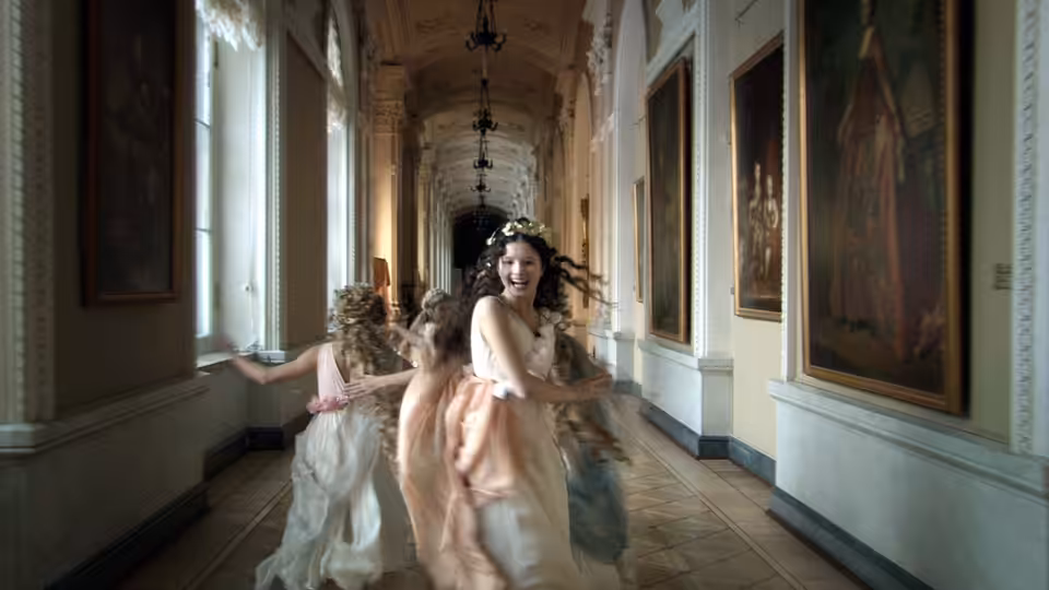 Young dancers in pastel dresses twirl through a gallery lined with paintings