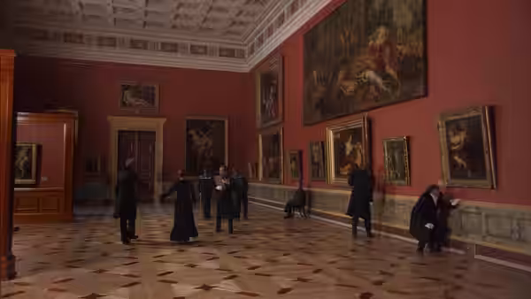 Visitors stand among paintings in a red-walled gallery