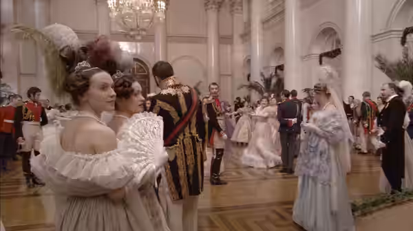 Guests in formal dress mingle and dance beneath chandeliers in a palace hall