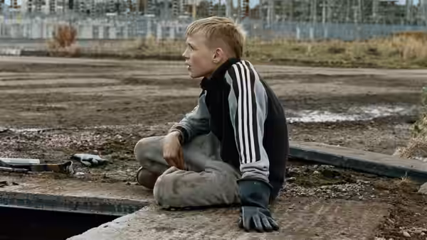 Blond boy sits on concrete in an empty industrial yard