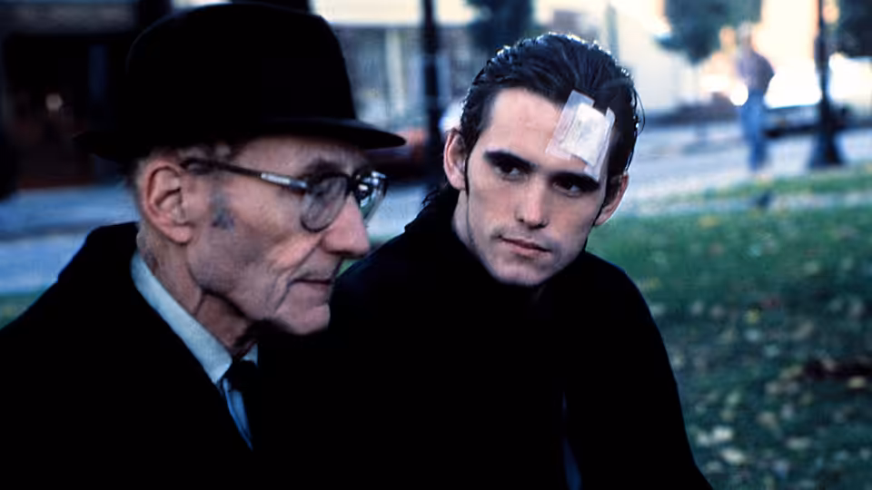 Tom the Priest (William S. Burroughs) sits beside Bob (Matt Dillon), who has a bandage on his forehead
