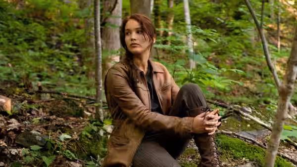 Katniss Everdeen (Jennifer Lawrence) seated on the forest floor looking aside