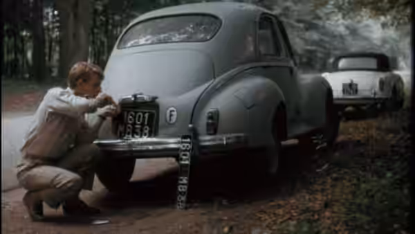 The Jackal (Edward Fox) examines the license plate of a gray car outdoors