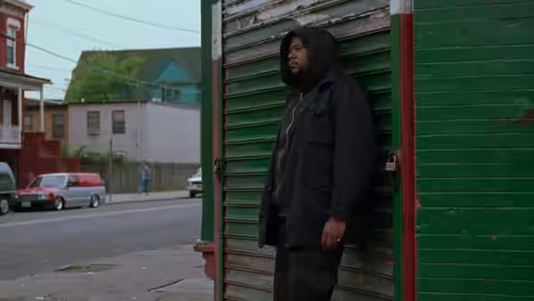 Ghost Dog (Forest Whitaker) leaning against a green metal shutter on a street