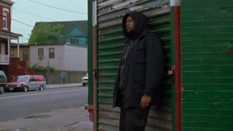 Ghost Dog (Forest Whitaker) leaning against a green metal shutter on a street