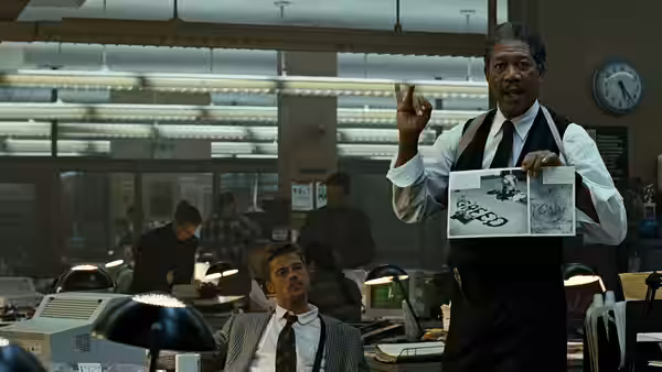 Somerset (Morgan Freeman) holds evidence photos in a police office as Mills sits nearby