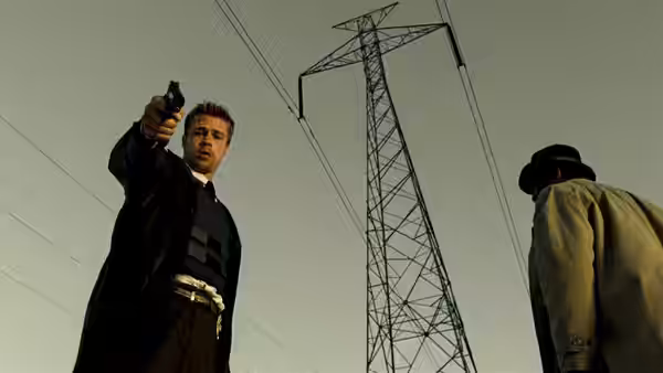 Mills (Brad Pitt) aims a handgun upward while Somerset stands nearby under power lines