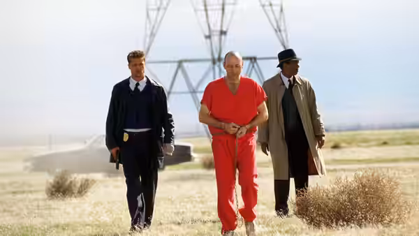 Mills (Brad Pitt), a man in red, and Somerset walk across open ground near towers