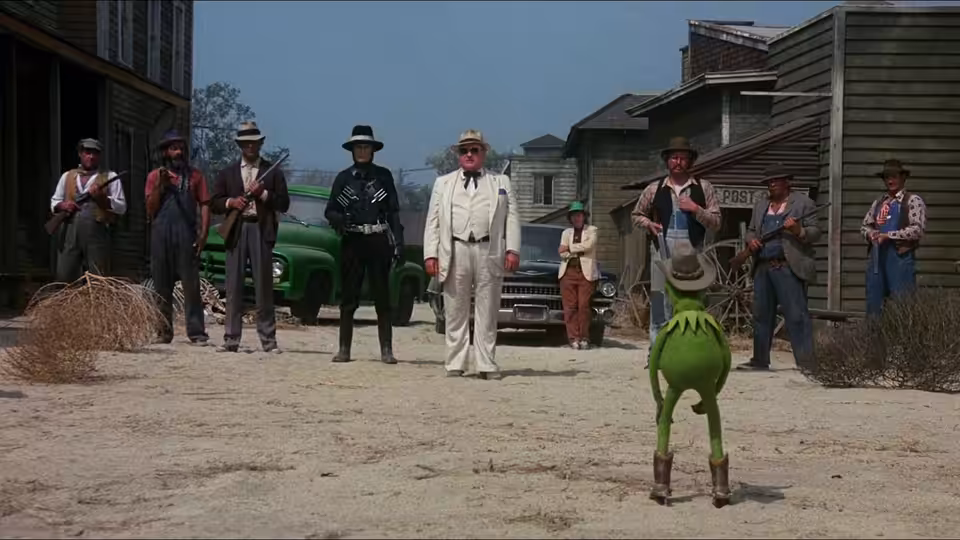 Kermit faces Doc Hopper (Charles Durning) and armed men in a dusty western town street