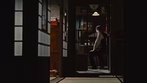 A man stands alone in a dim room beside shelves and a cabinet