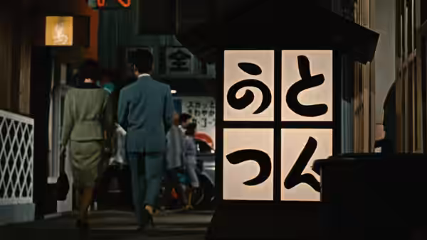 A man and woman walk through a city street past a large sign