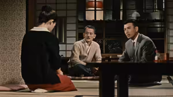 A woman kneels across a low table from two men in a traditional Japanese room
