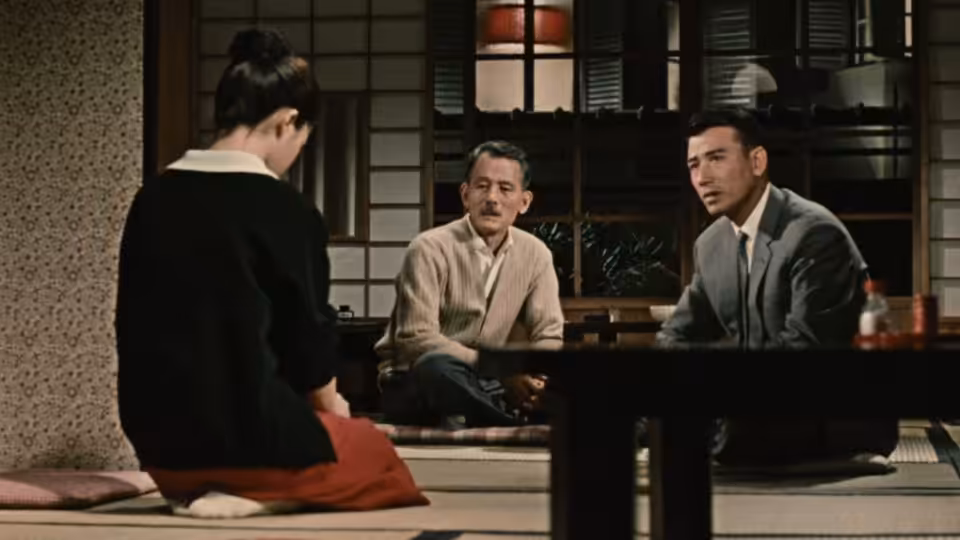 A woman kneels across a low table from two men in a traditional Japanese room