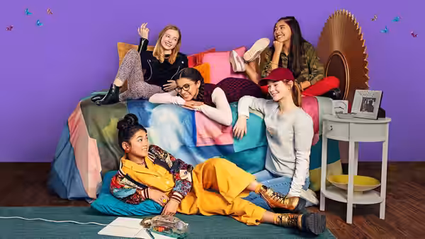 Claudia Kishi (Momona Tamada) lounges on the floor beside friends gathered on a bed