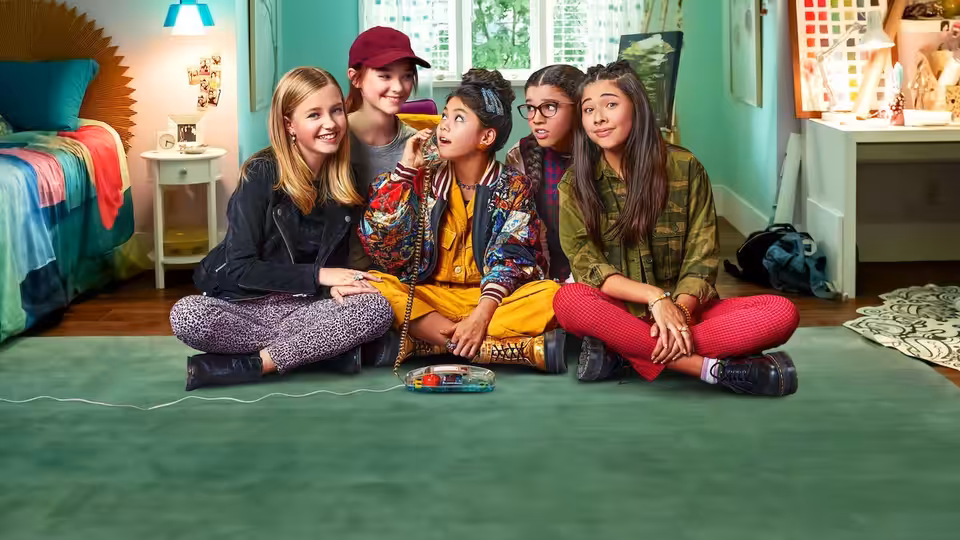 Five friends sit together on a bedroom floor around a board game