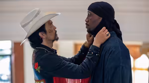 A man in a white cowboy hat adjusts another man's headscarf