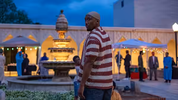 A man in a striped shirt stands beside a fountain in a busy outdoor plaza