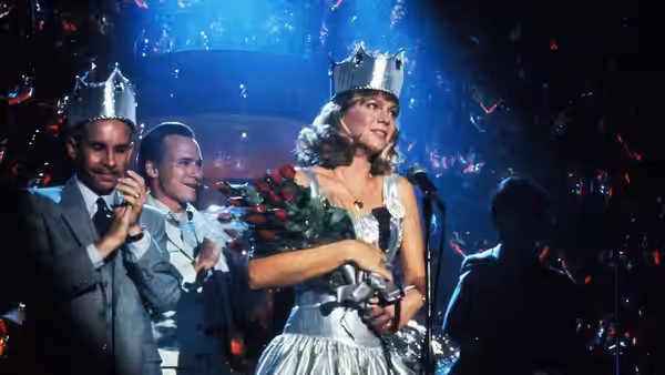 Peggy Sue (Kathleen Turner) wearing a crown and holding roses on stage
