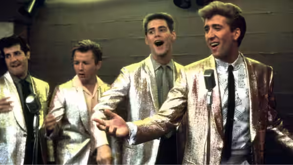Four performers in shiny jackets singing together on a stage