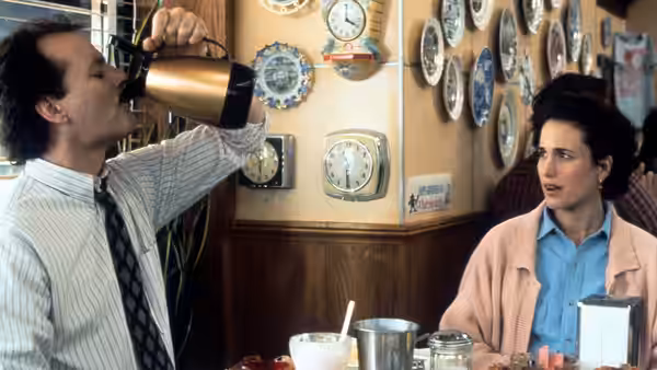 Phil Connors drinking from a coffee pot while Rita Hanson watches