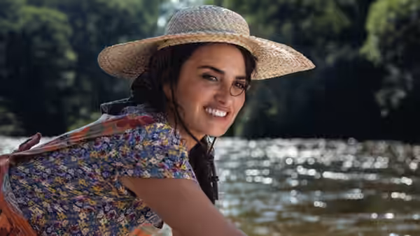 Smiling woman in straw hat and colorful blouse leans beside sunlit water