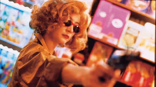 Woman in blonde wig aiming a gun in a convenience store