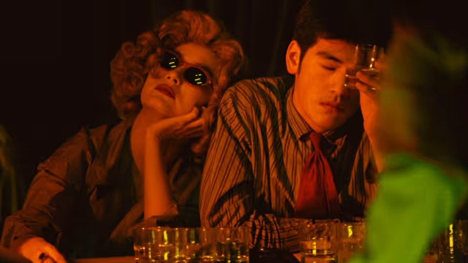 Woman in blonde wig and man in striped shirt at a bar counter