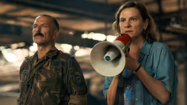 Aïda (Jasna Đuričić) speaks into a megaphone beside a mustached soldier