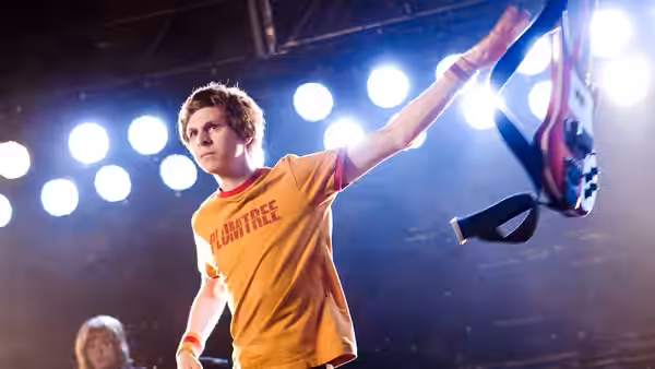 Scott Pilgrim (Michael Cera) raising a bass guitar on a brightly lit stage