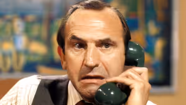 Reggie Perrin (Leonard Rossiter) speaks on a green telephone