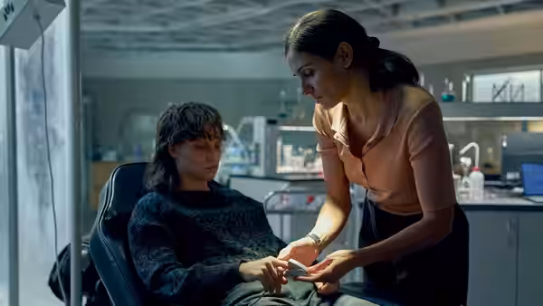 A woman hands a small item to a seated man in a clinical room