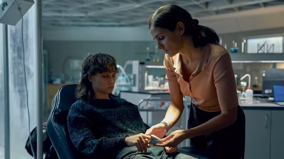 A woman hands a small item to a seated man in a clinical room