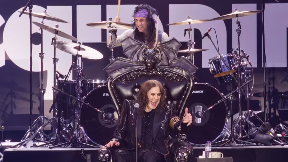 Ozzy Osbourne sits on a throne as Jason Momoa stands behind him onstage