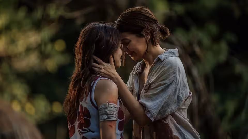 A woman cradles another woman's face as they stand close together outdoors