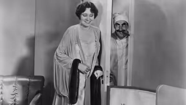 Margaret Dumont smiles near a doorway where a man in nightcap peeks out