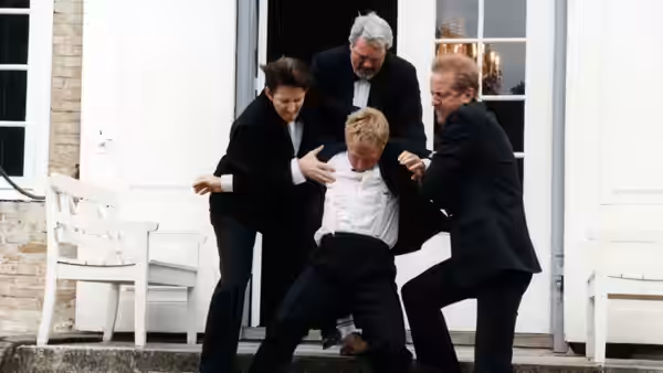 Men restraining Christian (Ulrich Thomsen) on the entrance steps