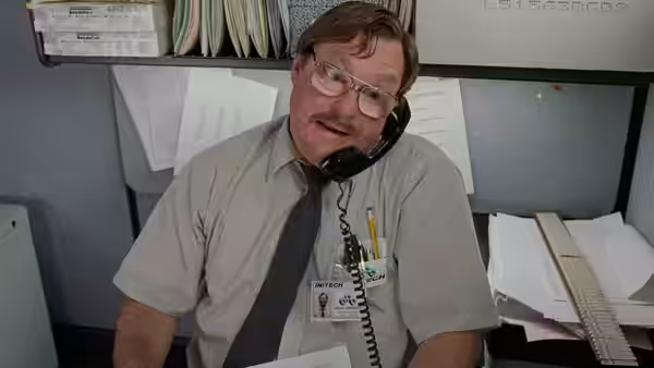 Milton (Stephen Root) speaking on the telephone at his cluttered desk
