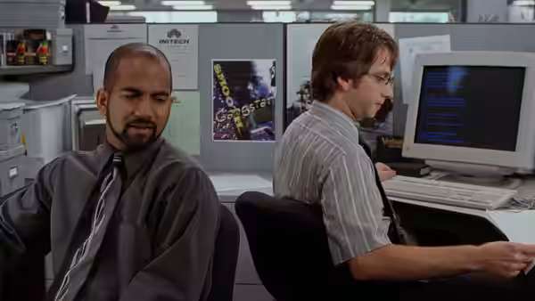 Samir (Ajay Naidu) and a colleague working at adjacent office desks