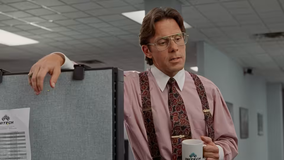 Bill Lumbergh (Gary Cole) leaning against a cubicle while holding a coffee mug