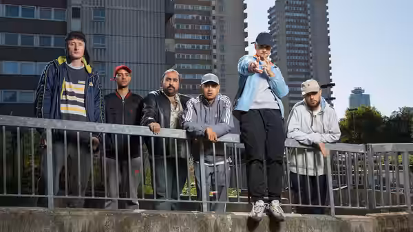 five men stand on a concrete ledge beside a railing with tall buildings behind