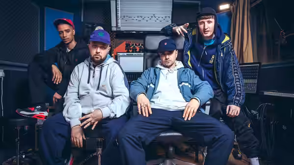 five men pose together in a music studio with one seated in the center
