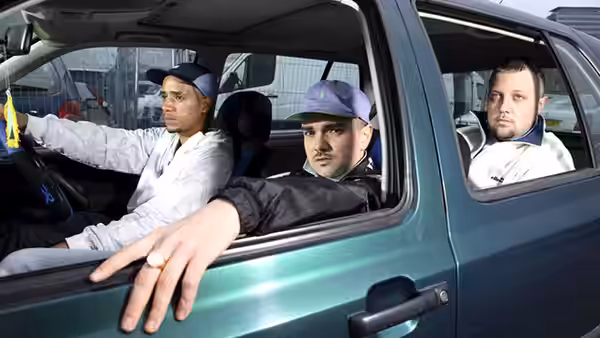 three men sit inside a green car with one leaning out the window