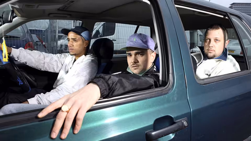 three men sit inside a green car with one leaning out the window